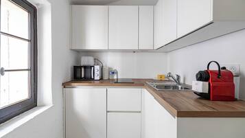 Una cocina compacta con armarios blancos, una encimera de madera, una cafetera, un hervidor y un electrodoméstico rojo, probablemente una aspiradora.