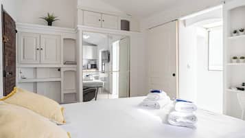 Habitación de hotel con cama, escritorio, silla, armario y baño visible a través de una puerta abierta.