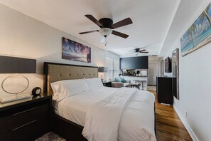 A bedroom with a bed, a nightstand, a ceiling fan, a painting, and a kitchenette in the background. - Savannah Apartment a Cozy Apartment Retreat Htd Pool and BBQ (West Palm Beach)