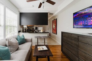 A modern living room with a sofa, coffee table, TV, and kitchen area. - Savannah Apartment a Cozy Apartment Retreat Htd Pool and BBQ (West Palm Beach)