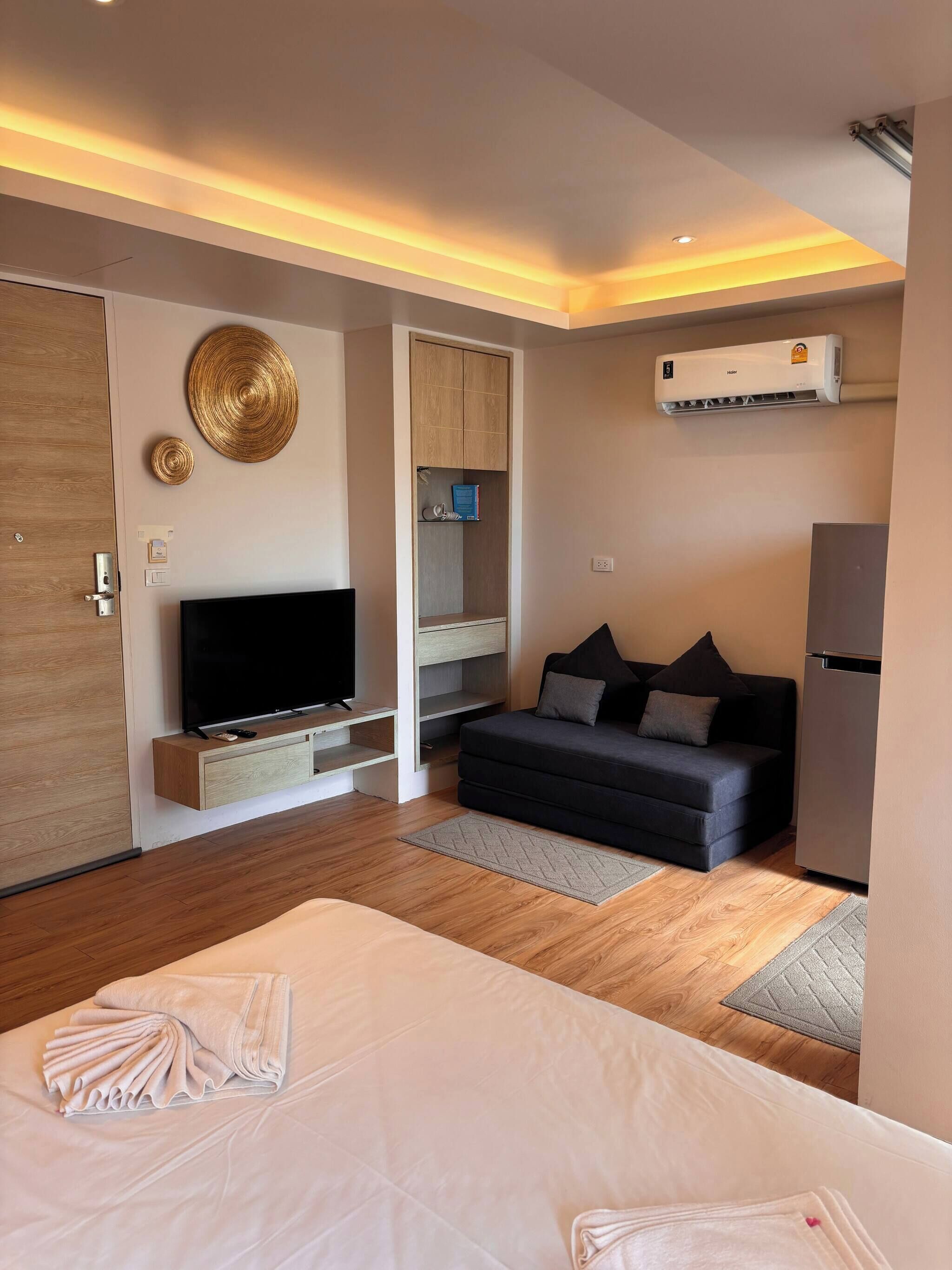 A modern hotel room with a flat-screen TV, a sofa, a bed, and a built-in wardrobe.
