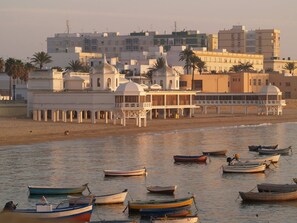 Zona costera con barcos en el agua, una playa y edificios al fondo.