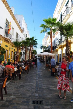Una calle estrecha con terrazas al aire libre, palmeras y edificios con balcones.