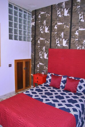 Un dormitorio con cama, cabecera roja, colcha estampada y manta roja.