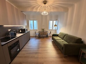 A modern kitchen with a dining area, a green sofa, and a chandelier. - Luxury Historic Apartment near Duomo & David (Firenze)