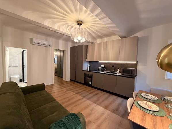 A modern kitchen with a chandelier, a dining area with plates and glasses, and a living room with a sofa. - Luxury Historic Apartment near Duomo & David (Firenze)