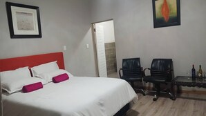 A hotel room with a bed, two chairs, a table with glasses and bottles, and a painting on the wall. - Room-serene Guest Room Retreat in Albert (Alberton)