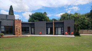 A modern two-story house with a flat roof, large windows, and a brick chimney. - Room-serene Guest Room Retreat in Albert (Alberton)