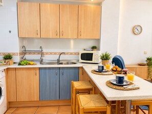 A compact kitchen with wooden cabinets, a microwave, a sink, and a breakfast setup with a cup, juice, and pastries. - Lentiscares 212 Beach & Pool – Torrox Costa (Torrox)