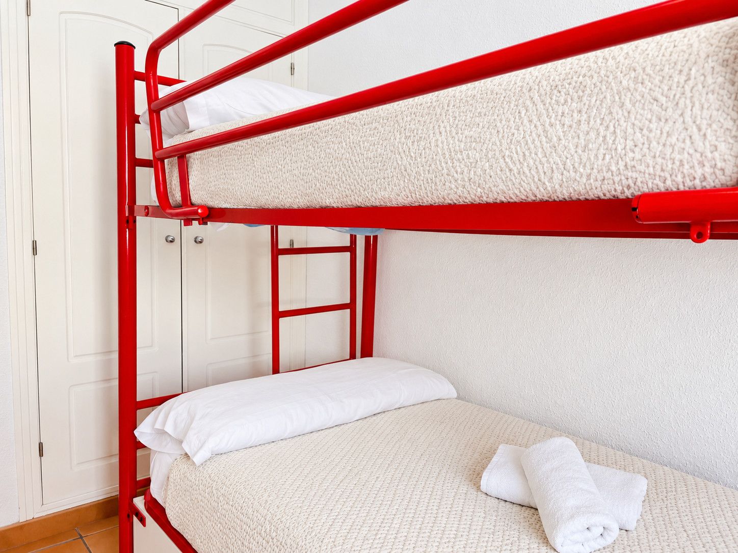 Ein Stockbett mit rotem Gestell, weißer Bettwäsche und einem Handtuch auf der unteren Liege.