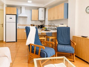 A compact kitchen with wooden cabinets, a built-in oven, and a water heater. There are two wooden chairs with blue cushions and a small table with a book. - Lentiscares 212 Beach & Pool – Torrox Costa (Torrox)