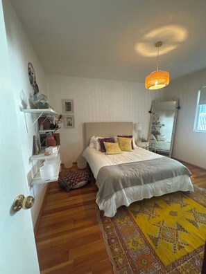 Ein Schlafzimmer mit einem Bett, einer Hängelampe, einem Spiegel und einem gemusterten Teppich.