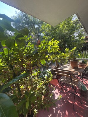 Ein überdachter Patio-Bereich mit Topfpflanzen, einem Holztisch und Stühlen.