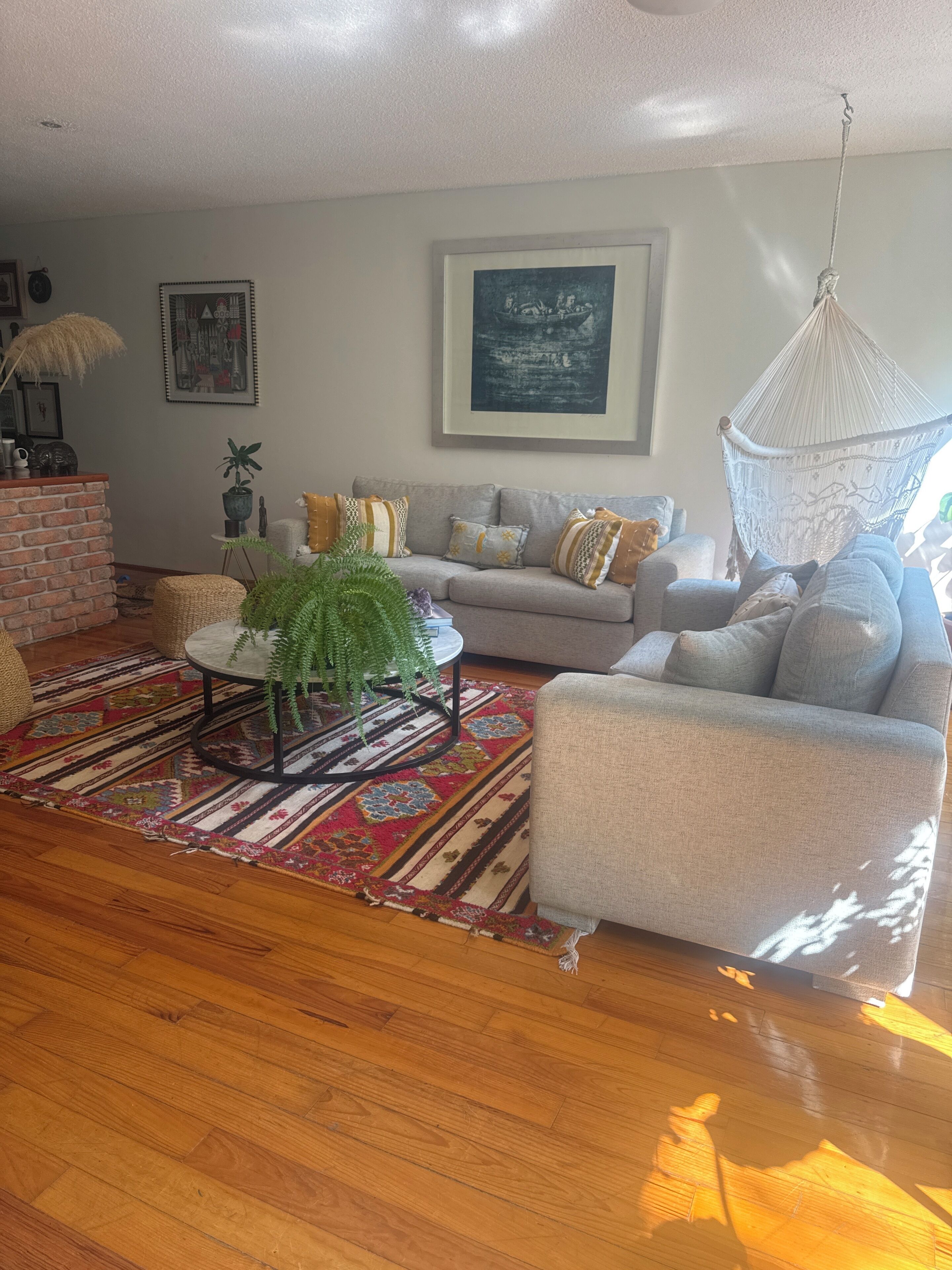 A living room with a sofa, a coffee table, a hanging chair, a patterned rug, and a brick accent wall.