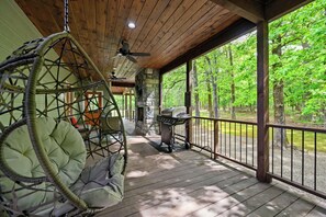 Eine Holzterrasse mit Hängesessel, Grill und Kamin aus Stein.
