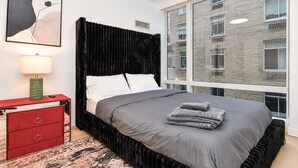 Un dormitorio moderno con un amplio ventanal, un cabecero negro y una mesita de noche roja.