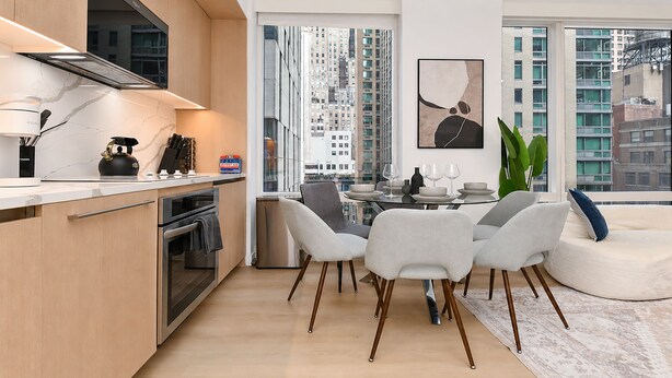 Una cocina moderna con horno integrado, un comedor con mesa redonda y sillas, y un ventanal con vistas a la ciudad.