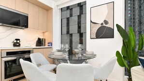 Una cocina moderna con electrodomésticos integrados, un comedor con mesa y sillas de vidrio, y un cuadro abstracto grande en la pared.
