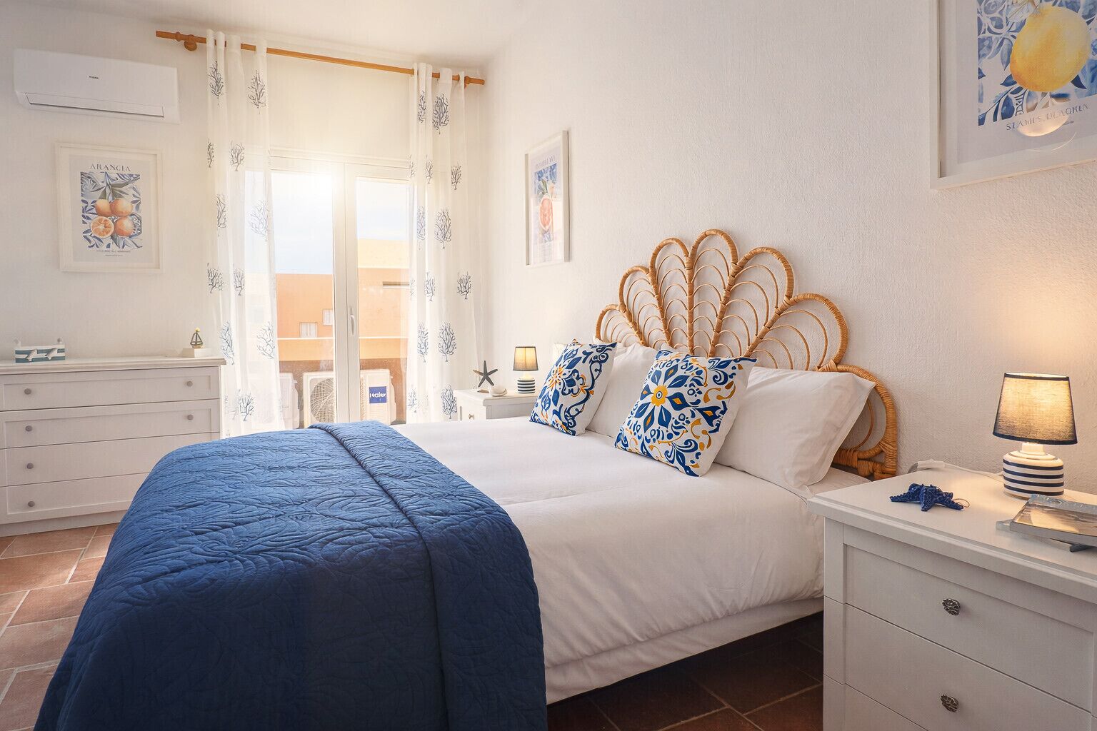 A bedroom with a bed, a nightstand, a lamp, a dresser, and a window with curtains.