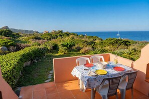 A terrace with a table set for four, overlooking a coastal landscape with vegetation and a clear sky. - Casa Audrey by Wonderful italy (Santa Teresa Gallura)