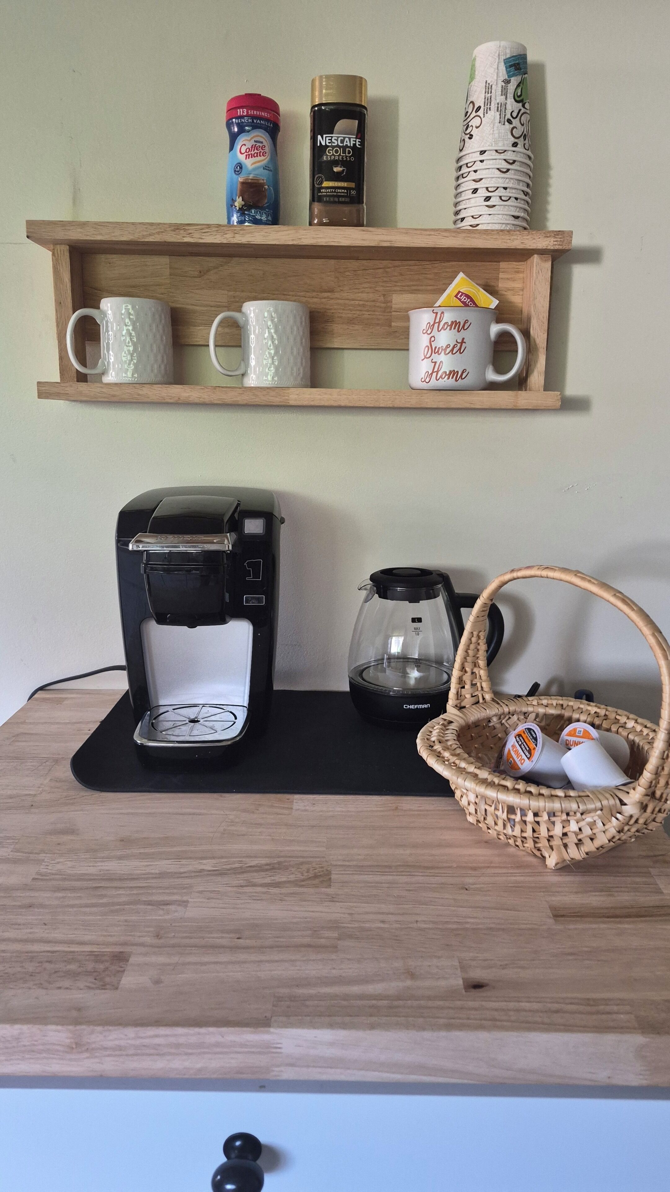 Angolo cottura con macchina per il caffè, bollitore, cestino con bustine di tè e scaffale con prodotti per il caffè e il tè.