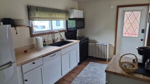 A compact kitchen with a refrigerator, microwave, sink, and a radiator. - The Borough Belle LLC -Spacious duplex in the heart of the historic district (Ebensburg)