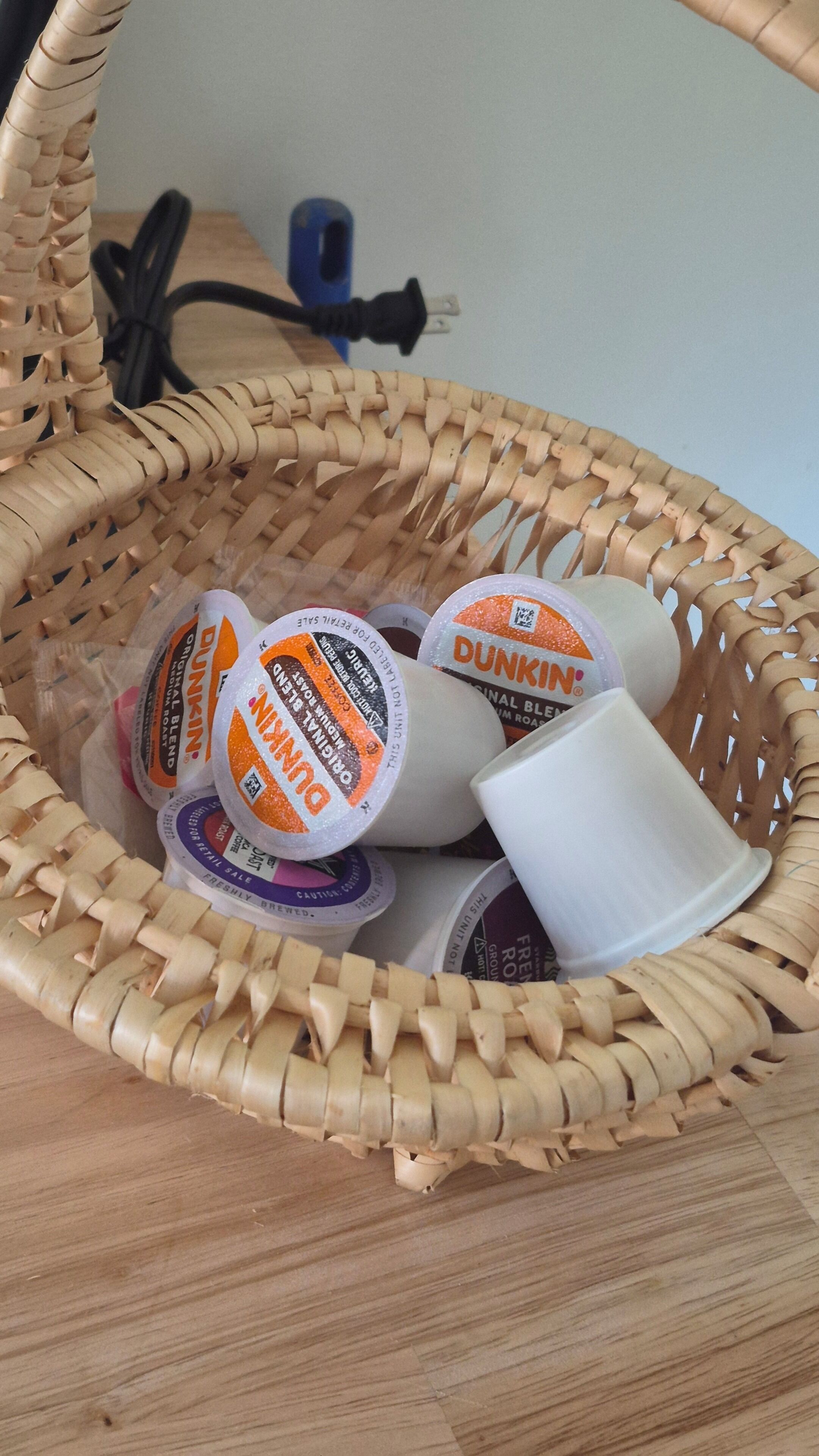 Un panier en osier contenant des gobelets à café de la chaîne Dunkin' Donuts et un gobelet en papier blanc.