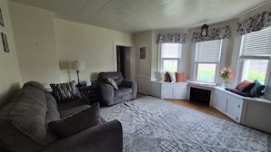 A living room with a sofa, a coffee table, a lamp, and a window with a view. - The Borough Belle LLC -Spacious duplex in the heart of the historic district (Ebensburg)