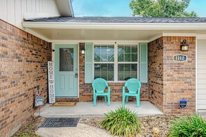 A brick house with a green door, two turquoise chairs outside, and a mailbox.