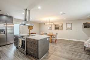 A kitchen with a central island, stainless steel appliances, and a dining area with chairs and a table.