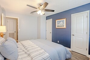 A bedroom with a bed, a ceiling fan, a framed picture, and two doors.