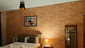 Ein Schlafzimmer mit Backsteinwand, einem Bett, einem Nachttisch mit Lampe und einem Spiegel.