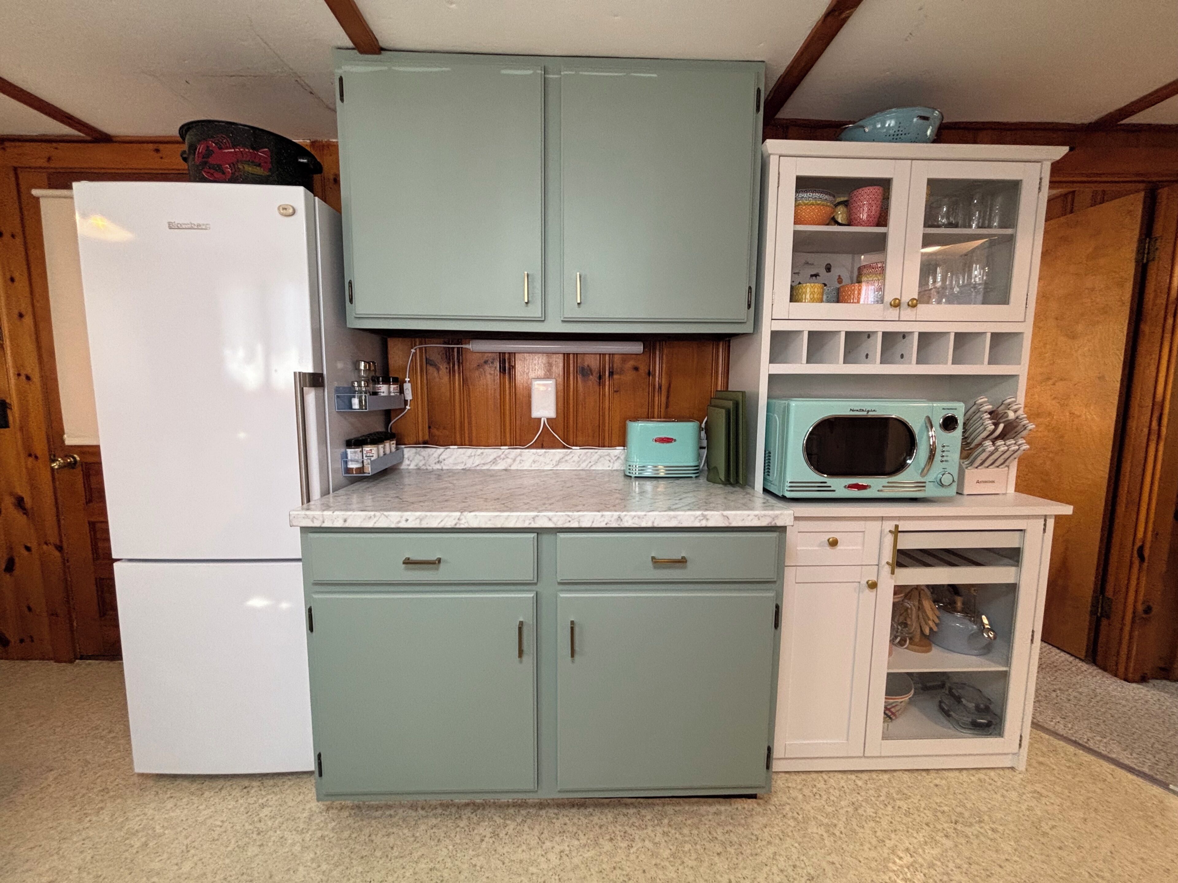 A kitchen with a refrigerator, cabinets, a microwave, and a shelf with kitchen utensils.