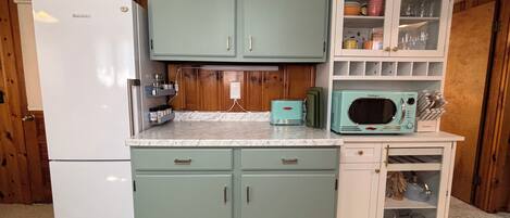 A kitchen with a refrigerator, cabinets, a microwave, and a shelf with kitchen utensils.