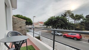 A balcony with a table and chairs, a street view with cars, and a clear sky. - NAUSICA (Saint-Jean-de-Monts)