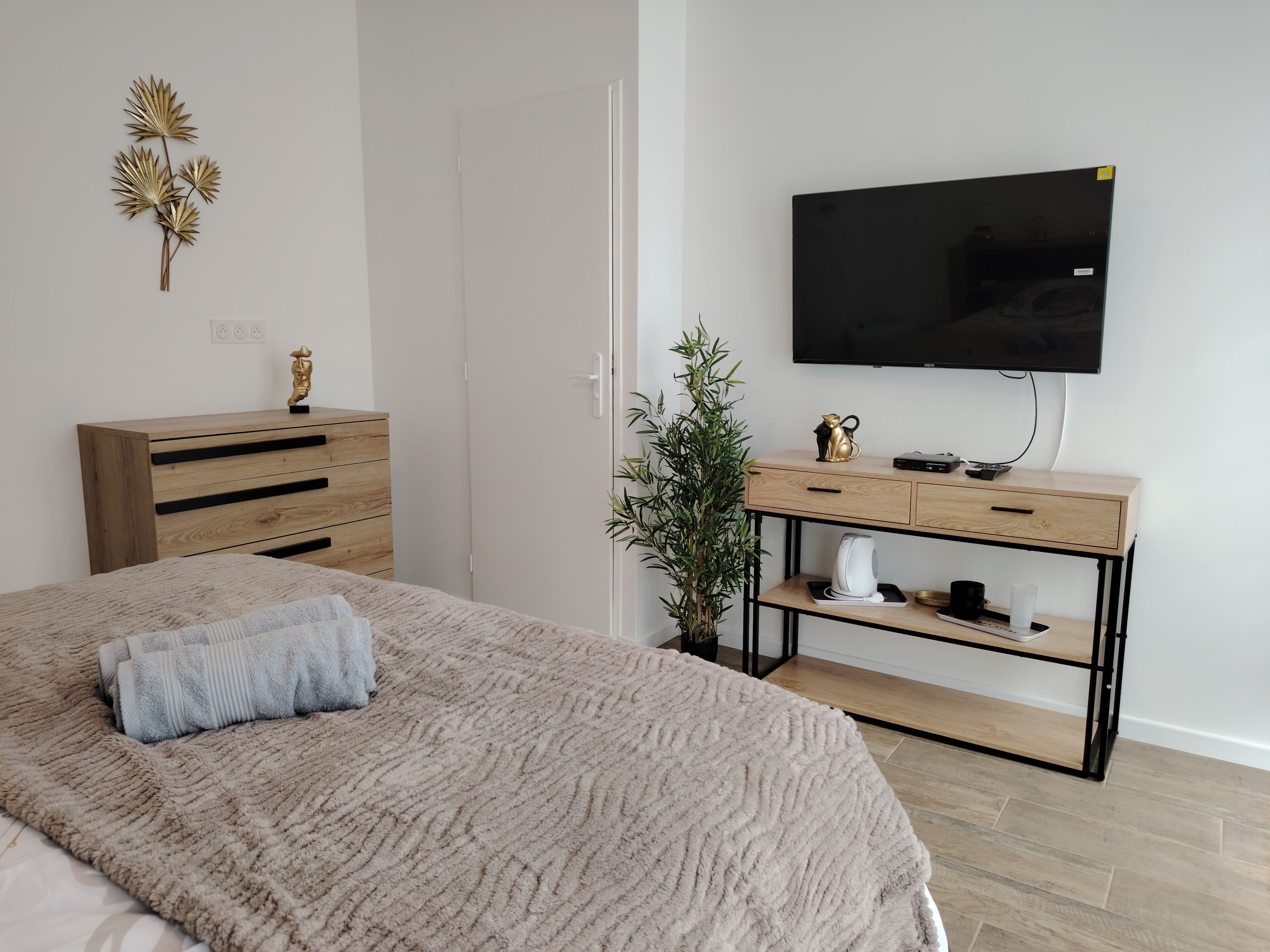 Une chambre à coucher comprenant un lit, une commode, un téléviseur, une plante et une console sur laquelle se trouve une machine à café.