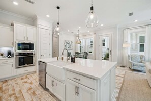 A spacious kitchen with white cabinetry, a large island, stainless steel appliances, pendant lighting, and a dining area with a view.
