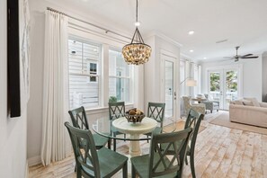 A dining area with a glass table, green chairs, a chandelier, and a view of the outside.