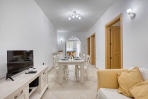 Ein modernes Wohnzimmer mit Flachbildfernseher, Esstisch mit Stühlen, einer Couch und einer Holztür.