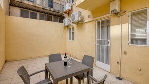 En lille udendørs terrasse med et bord, stole, en vinflaske og to vinglas.
