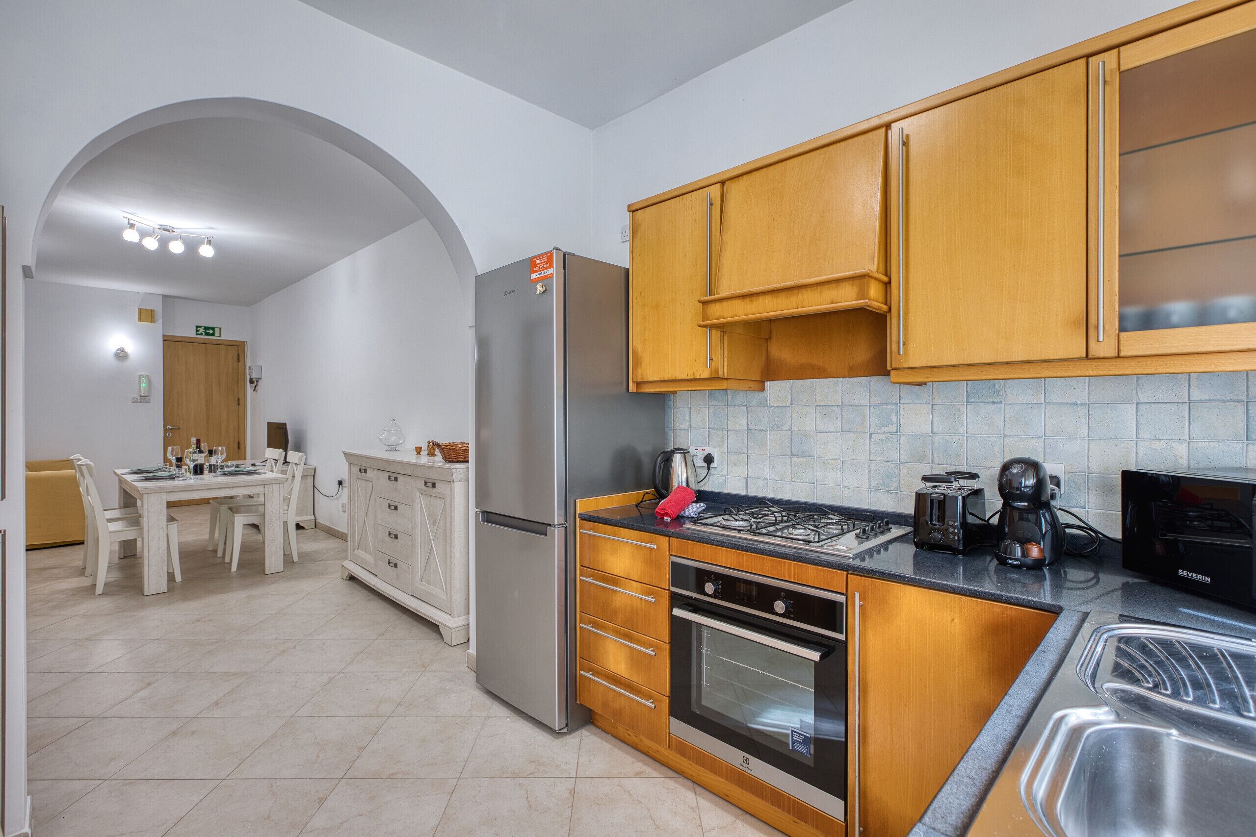 Una cocina moderna con electrodomésticos de acero inoxidable, armarios de madera, un comedor con mesa y sillas, y salpicadero de azulejos.