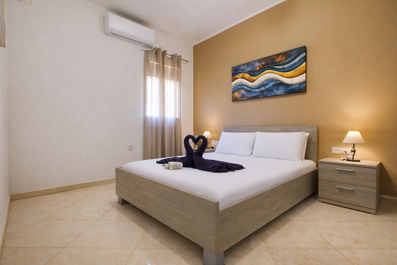 Een hotelkamer met een bed, nachtkastje, lamp, schilderij aan de muur en een airconditioning.