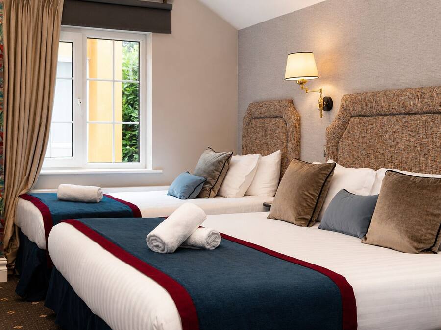 A hotel room with two beds, a window with curtains, a wall-mounted lamp, and a patterned headboard.