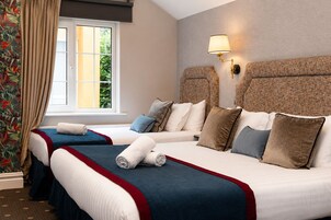 A hotel room with two beds, a window with curtains, a wall-mounted lamp, and a patterned headboard.