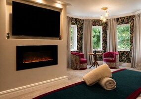 A room with a fireplace, a television, two chairs, a table, and a window with curtains.