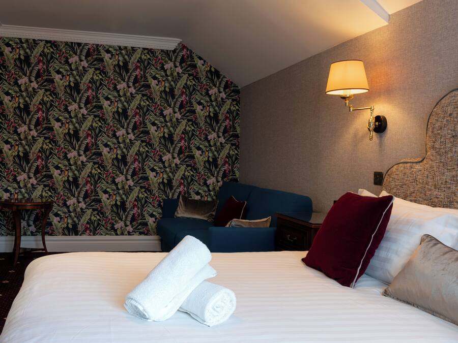 A hotel room with a bed, a blue sofa, a nightstand, a lamp, and a floral wallpaper.