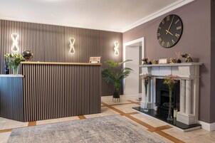 A reception area with a wooden reception desk, a large wall clock, and a fireplace with decorative items.
