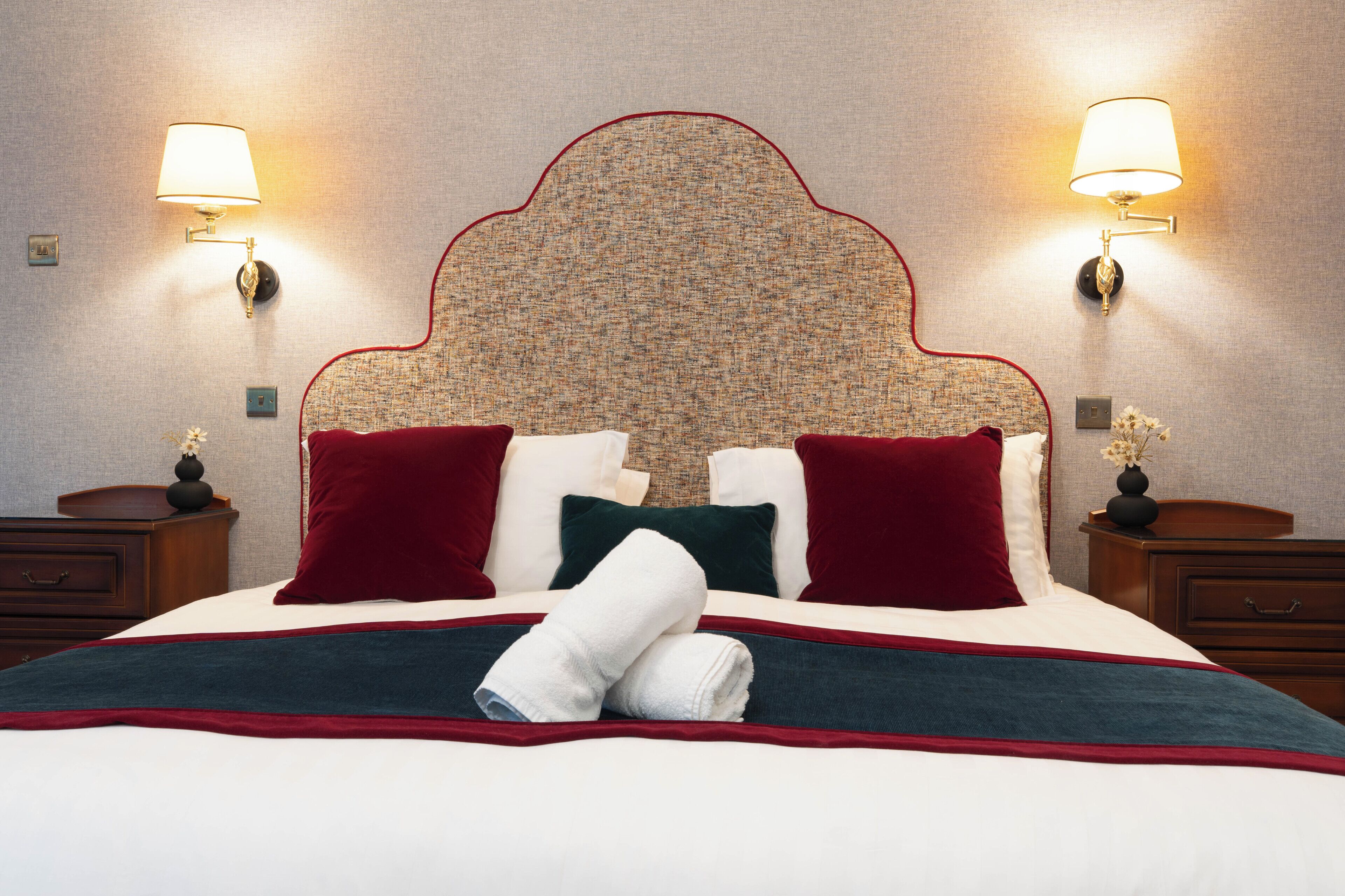 A hotel room with a large bed, two nightstands, a headboard with a patterned design, and wall-mounted lamps.