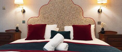 A hotel room with a large bed, two nightstands, a headboard with a patterned design, and wall-mounted lamps.