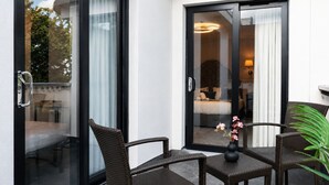 Une chambre d’hôtel dotée d’une porte-fenêtre coulissante donnant sur un balcon, aménagé avec des fauteuils en osier et une petite table.